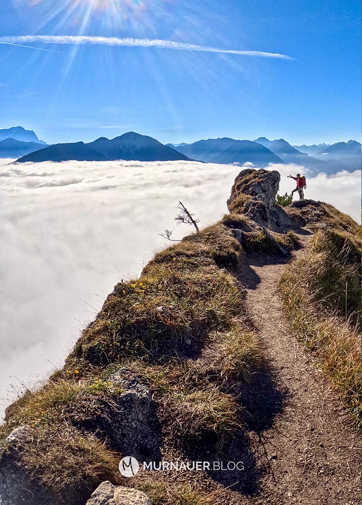 Zwei Wanderer erklären sich das Bergpanorma in der Ferne, sie stehen über einem Nebelmeer bei blauen Himmel